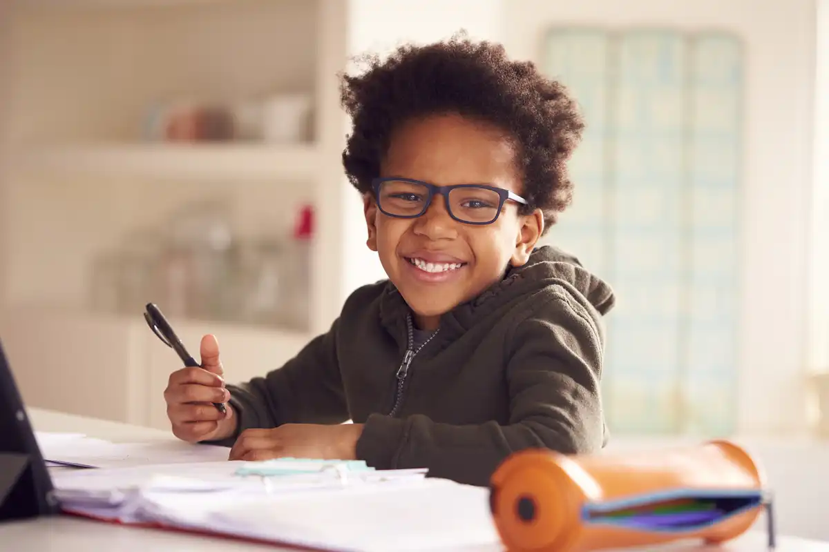 Boy sitting down with school work smiling.