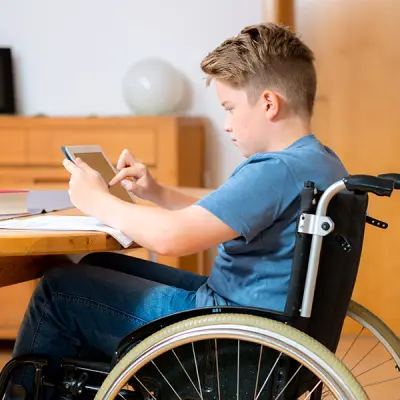 Boy sitting in a wheelchair working on a tablet.